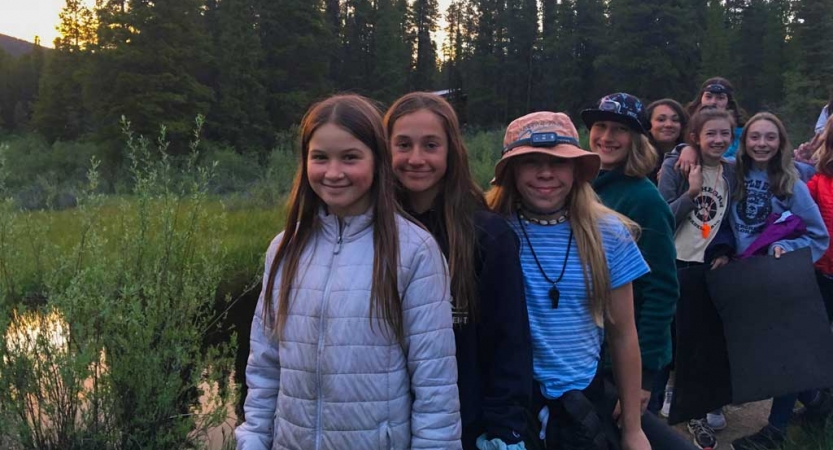 A group of people smile in a green area with trees in the background. 